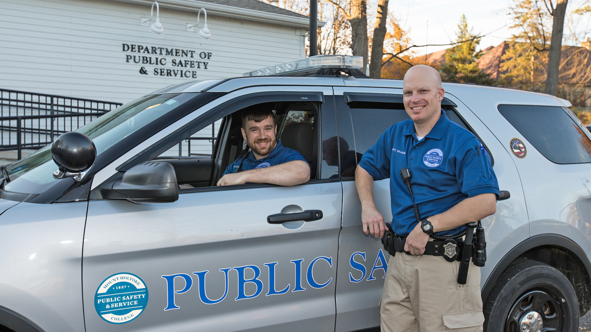 Two public safety offices -  one seated in a car the other leaning on the car