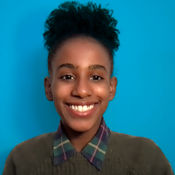 Dinanyelin Martinez ’24, wearing a green sweater with plaid collar, smiles at the camera.